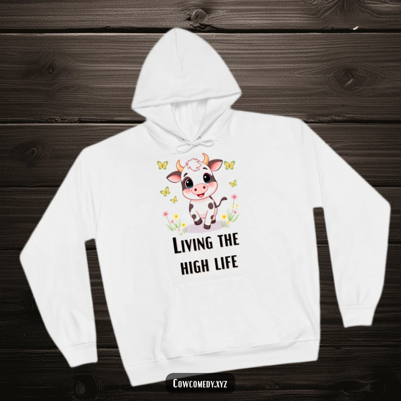 Funny hoodie depicting a happy cow bounding through a meadow, playfully chasing an array of colorful butterflies with evident glee and happiness.